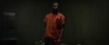 Movie still from “Without Remorse” (2021), directed by Stefano Sollima – A man in an orange shirt standing in a dark room; Medium shot, Low angle