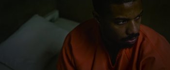 Movie still from “Without Remorse” (2021), directed by Stefano Sollima – A man in a red shirt sitting in front of a white wall; Close Up shot, High angle