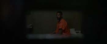 Movie still from “Without Remorse” (2021), directed by Stefano Sollima – A man in an orange shirt sitting on a bed in a jail cell; Wide shot, High angle
