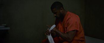 Movie still from “Without Remorse” (2021), directed by Stefano Sollima – A man in a red jumpsuit is holding a white bag; Medium shot, High angle