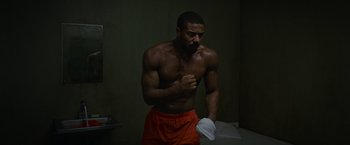 Movie still from “Without Remorse” (2021), directed by Stefano Sollima – A man in orange shorts holding a white towel; Medium shot, High angle