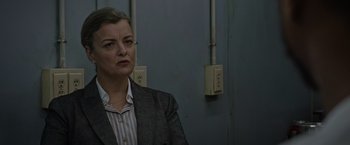 Movie still from “Without Remorse” (2021), directed by Stefano Sollima – A woman wearing a suit and striped shirt is standing in front of a wall; Close Up shot, Over the shoulder angle