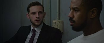 Movie still from “Without Remorse” (2021), directed by Stefano Sollima – A man in a suit and tie standing next to another man in a suit and tie; Close Up shot, Over the shoulder angle