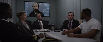 Movie still from “Without Remorse” (2021), directed by Stefano Sollima – A group of men sitting at a table in front of a tv; Medium shot, Over the shoulder angle