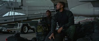 Movie still from “Without Remorse” (2021), directed by Stefano Sollima – A man sitting next to another man with a backpack; Medium shot, Low angle