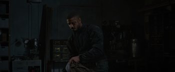 Movie still from “Without Remorse” (2021), directed by Stefano Sollima – A man holding a bag in a dark room; Medium shot, Low angle