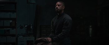 Movie still from “Without Remorse” (2021), directed by Stefano Sollima – A man standing in a dark room with his arms crossed; Medium shot, Low angle