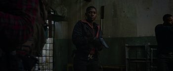 Movie still from “Without Remorse” (2021), directed by Stefano Sollima – A man holding a gun while standing next to a wall; Medium shot, Low angle