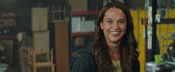 Movie still from “Tomb Raider” (2018), directed by Roar Uthaug – A woman smiling for the camera in a warehouse; Close Up shot, Over the shoulder angle