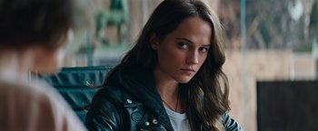 Movie still from “Tomb Raider” (2018), directed by Roar Uthaug – A beautiful young woman with long brown hair wearing a leather jacket; Close Up shot, Over the shoulder angle