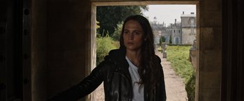Movie still from “Tomb Raider” (2018), directed by Roar Uthaug – A beautiful young woman wearing a black jacket; Close Up shot, Over the shoulder angle