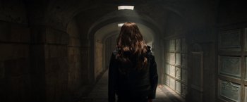 Movie still from “Tomb Raider” (2018), directed by Roar Uthaug – A woman with long brown hair walking down a dark hallway; Medium shot, Over the shoulder angle