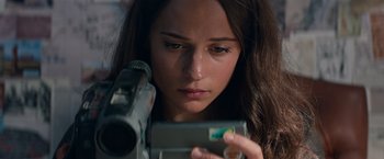Movie still from “Tomb Raider” (2018), directed by Roar Uthaug – A woman holding a video camera looking at the camera; Close Up shot, High angle