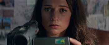 Movie still from “Tomb Raider” (2018), directed by Roar Uthaug – A woman looking at the camera while holding a cell phone; Close Up shot, Low angle