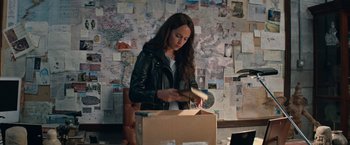 Movie still from “Tomb Raider” (2018), directed by Roar Uthaug – A woman in a leather jacket looking at an open cardboard box; Medium shot, High angle
