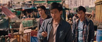 Movie still from “Tomb Raider” (2018), directed by Roar Uthaug – Two young men standing next to each other in a market; Medium shot, Over the shoulder angle