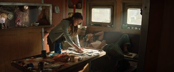 Movie still from “Tomb Raider” (2018), directed by Roar Uthaug – A woman cutting papers on a table in a living room; Medium shot, High angle
