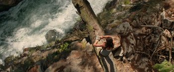 Movie still from “Tomb Raider” (2018), directed by Roar Uthaug – A woman sitting next to a tree on a cliff looking at the water; Wide shot, Overhead angle