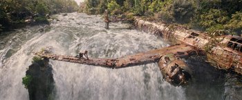 Movie still from “Tomb Raider” (2018), directed by Roar Uthaug – A man sitting on top of a log in the middle of a river; Extreme Wide shot, High angle