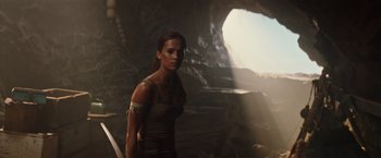 Movie still from “Tomb Raider” (2018), directed by Roar Uthaug – A woman standing next to a cave in the dark; Medium shot, Low angle