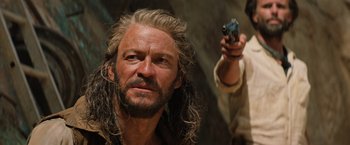 Movie still from “Tomb Raider” (2018), directed by Roar Uthaug – A man with long grey hair and a beard holding a gun; Close Up shot, Over the shoulder angle