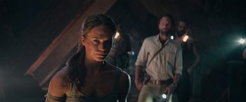 Movie still from “Tomb Raider” (2018), directed by Roar Uthaug – A man and a woman standing next to each other in a room; Close Up shot, Over the shoulder angle