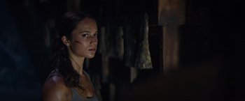 Movie still from “Tomb Raider” (2018), directed by Roar Uthaug – A woman with a scar on her face standing in a dark room; Close Up shot, Over the shoulder angle