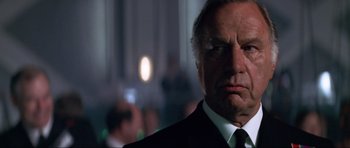 Movie still from “Tomorrow Never Dies” (1997), directed by Roger Spottiswoode – A man in a suit and tie looking at the camera; Close Up shot, Low angle