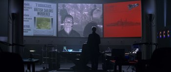 Movie still from “Tomorrow Never Dies” (1997), directed by Roger Spottiswoode – A man standing in front of a projector screen; Medium shot, Over the shoulder angle