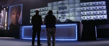Movie still from “Tomorrow Never Dies” (1997), directed by Roger Spottiswoode – Two men standing in front of a video wall; Medium shot, Over the shoulder angle
