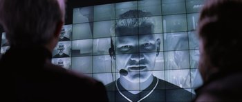 Movie still from “Tomorrow Never Dies” (1997), directed by Roger Spottiswoode – A man with a microphone in front of a video wall; Close Up shot, Low angle
