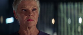 Movie still from “Tomorrow Never Dies” (1997), directed by Roger Spottiswoode – An older woman with short white hair looking at the camera; Close Up shot, Low angle