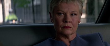 Movie still from “Tomorrow Never Dies” (1997), directed by Roger Spottiswoode – An older woman sitting in a chair looking at the camera; Close Up shot, Low angle