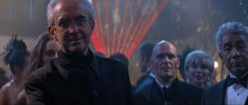 Movie still from “Tomorrow Never Dies” (1997), directed by Roger Spottiswoode – A man in a suit and tie standing next to another man in a suit and tie; Close Up shot, Over the shoulder angle
