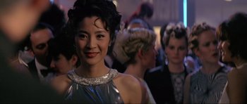 Movie still from “Tomorrow Never Dies” (1997), directed by Roger Spottiswoode – A woman in a silver dress standing next to other people; Close Up shot, Over the shoulder angle