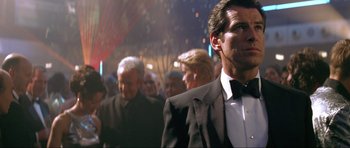 Movie still from “Tomorrow Never Dies” (1997), directed by Roger Spottiswoode – A man in a tuxedo standing next to a crowd of people; Medium shot, Over the shoulder angle