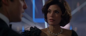 Movie still from “Tomorrow Never Dies” (1997), directed by Roger Spottiswoode – A woman wearing a black dress and a necklace; Close Up shot, Over the shoulder angle