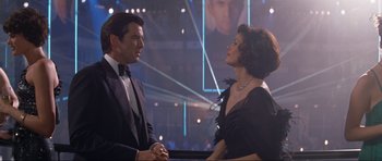 Movie still from “Tomorrow Never Dies” (1997), directed by Roger Spottiswoode – A man and a woman are talking to each other in front of an audience; Medium shot, Over the shoulder angle
