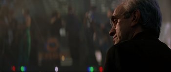 Movie still from “Tomorrow Never Dies” (1997), directed by Roger Spottiswoode – An older man wearing glasses looking off into the distance; Close Up shot, Over the shoulder angle