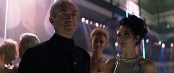Movie still from “Tomorrow Never Dies” (1997), directed by Roger Spottiswoode – A man and two women standing next to each other in front of lights; Close Up shot, Over the shoulder angle