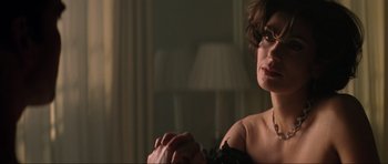 Movie still from “Tomorrow Never Dies” (1997), directed by Roger Spottiswoode – A woman sitting in front of a lamp in a room; Close Up shot, Over the shoulder angle