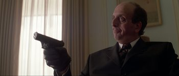 Movie still from “Tomorrow Never Dies” (1997), directed by Roger Spottiswoode – An older man in a suit and tie holding a glove; Close Up shot, Low angle