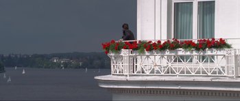 Movie still from “Tomorrow Never Dies” (1997), directed by Roger Spottiswoode – A person sitting on a balcony with flowers; Wide shot, Low angle