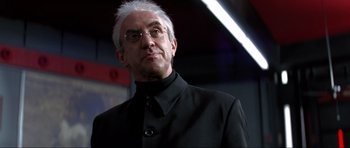 Movie still from “Tomorrow Never Dies” (1997), directed by Roger Spottiswoode – An older man in a black suit and white hair; Close Up shot, Low angle