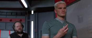 Movie still from “Tomorrow Never Dies” (1997), directed by Roger Spottiswoode – A man with blonde hair is holding a pair of scissors in his hand; Close Up shot, Low angle