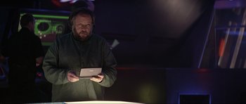 Movie still from “Tomorrow Never Dies” (1997), directed by Roger Spottiswoode – A man holding an ipad while standing in front of a table; Medium shot, Low angle