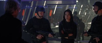 Movie still from “Tomorrow Never Dies” (1997), directed by Roger Spottiswoode – A man and a woman are standing next to each other holding guns; Medium shot, Over the shoulder angle