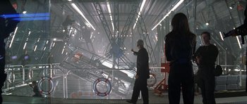 Movie still from “Tomorrow Never Dies” (1997), directed by Roger Spottiswoode – A man in a black suit is pointing to a ship in the background; Wide shot, High angle