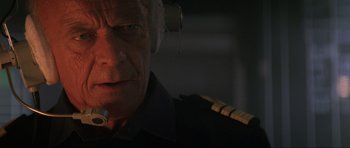 Movie still from “Tomorrow Never Dies” (1997), directed by Roger Spottiswoode – An older man wearing a pilot's uniform and headphones; Close Up shot, Low angle