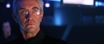 Movie still from “Tomorrow Never Dies” (1997), directed by Roger Spottiswoode – An older man wearing glasses and a black shirt; Close Up shot, Over the shoulder angle